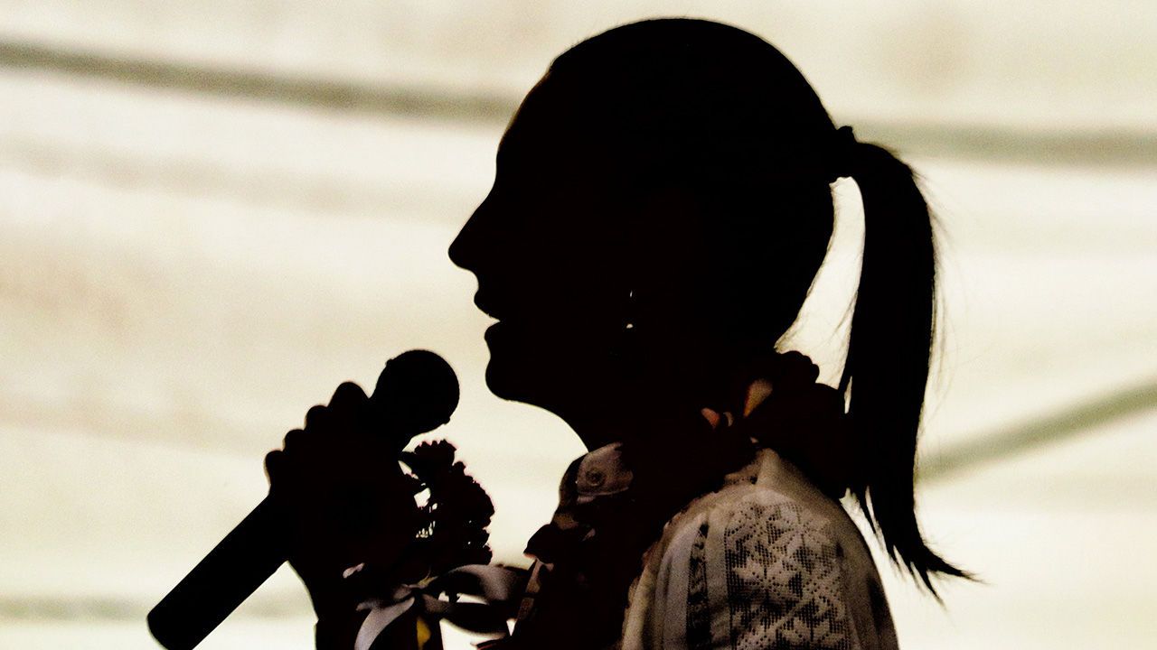 A silhouetted profile of Claudia Sheinbaum speaking into a microphone.