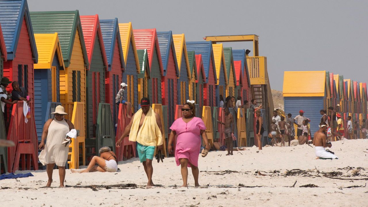 People in front of the colourful bathing huts at Muizenberg Beach, near Cape Town